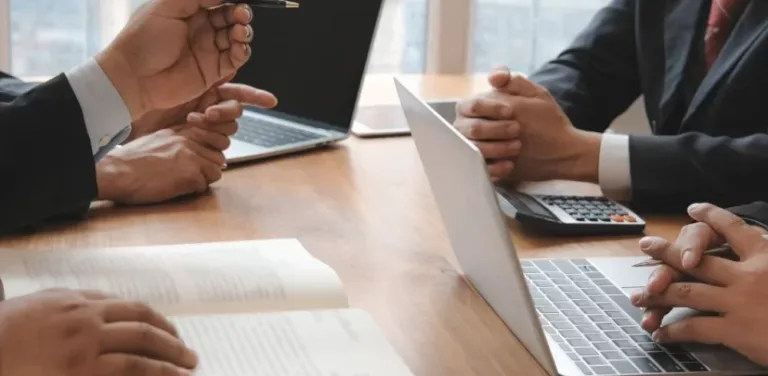 Business meeting with lawyers working on laptops and documents at conference table.