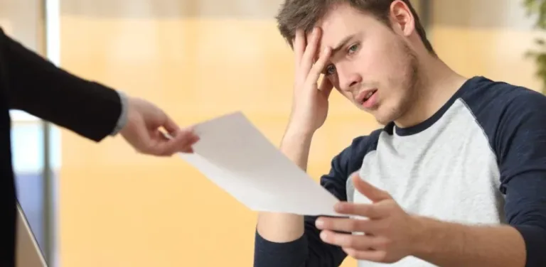 Worried young man holding a document as someone hands him paperwork, looking stressed.