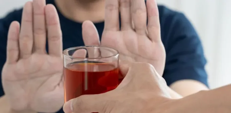 Person raising both hands to refuse an offered glass of alcohol.