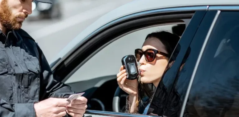 Female driver blowing into breathalyzer during roadside DUI stop with police officer.