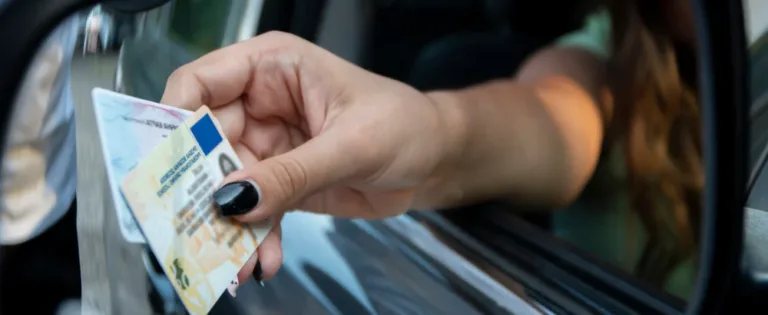 Woman with black nail polish handing driver’s license and ID cards out of car window.