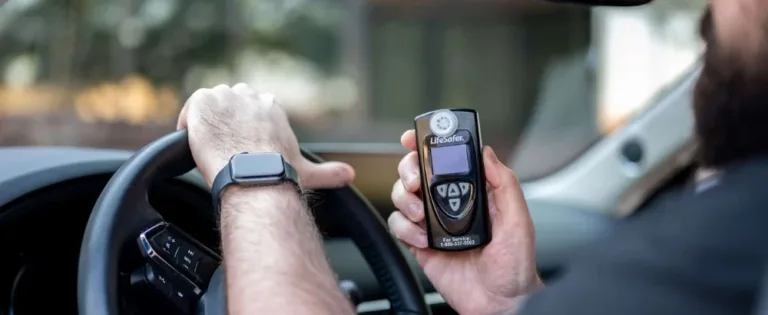 Driver in car holding an ignition interlock device while hand rests on steering wheel
