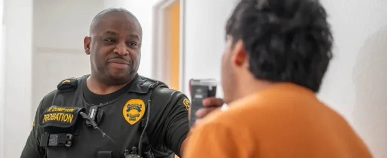 Probation officer holding breathalyzer device in front of man during alcohol test.
