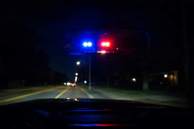 Police emergency lights reflected in a car rearview mirror on a dark Michigan road at night